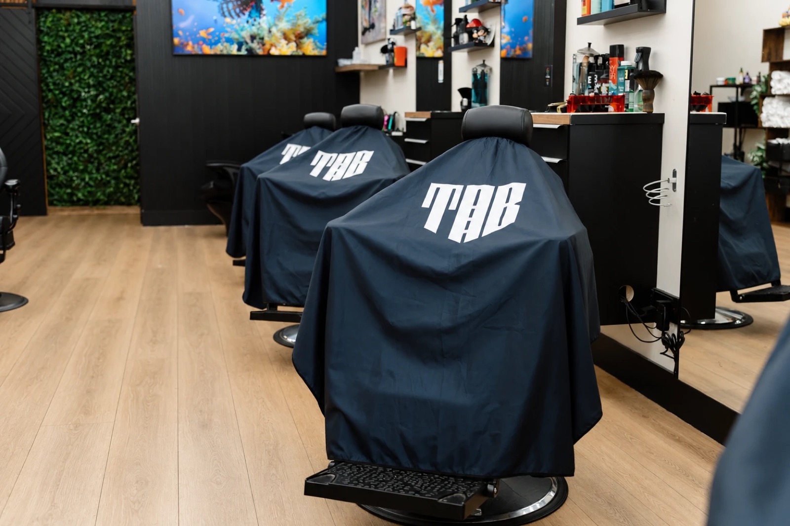 Barber chairs at The Avenue Barbershop draped in navy capes printed with the TAB logo